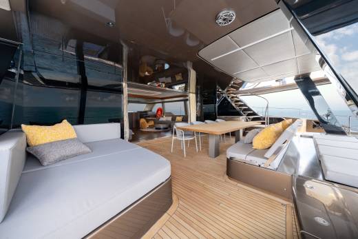 A luxurious yacht deck with comfortable seating and a dining area in the foreground, and the ocean and sky visible in the background.