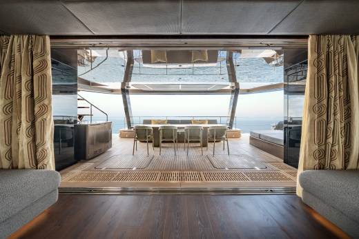 A luxurious yacht's open deck with a dining table and seating in the foreground, and the ocean stretching to the horizon in the background.