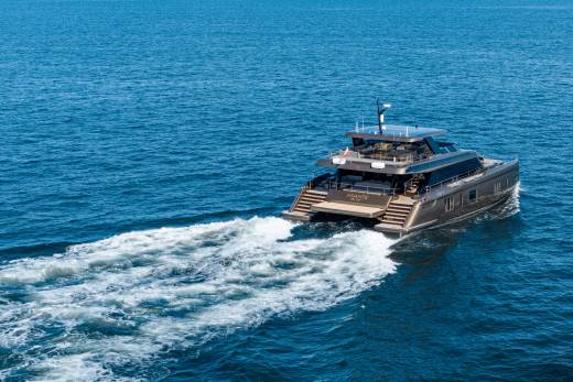A sleek, modern catamaran yacht cruises through calm blue waters, leaving a foamy white wake behind it.