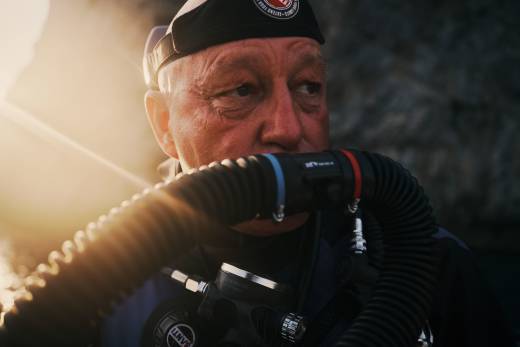 A diver wearing a black cap and breathing apparatus is positioned in the foreground against a blurred, rocky background.