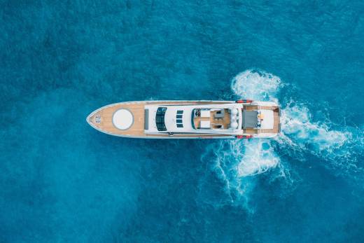 A white motor yacht cruises through deep blue ocean water, leaving a trail of white foam in its wake.