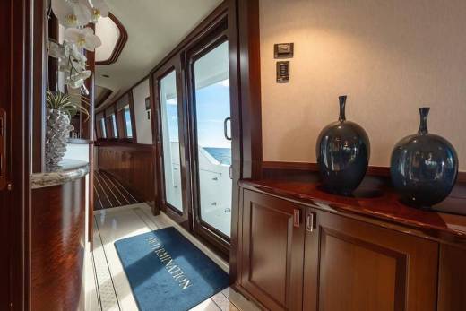 Two dark blue vases sit on a polished wooden cabinet in the foreground, with a hallway leading to an open door that reveals a bright ocean view in the background.