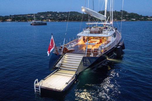 A luxury yacht with a lowered swim platform floats in deep blue water against a backdrop of a distant, hilly coastline.