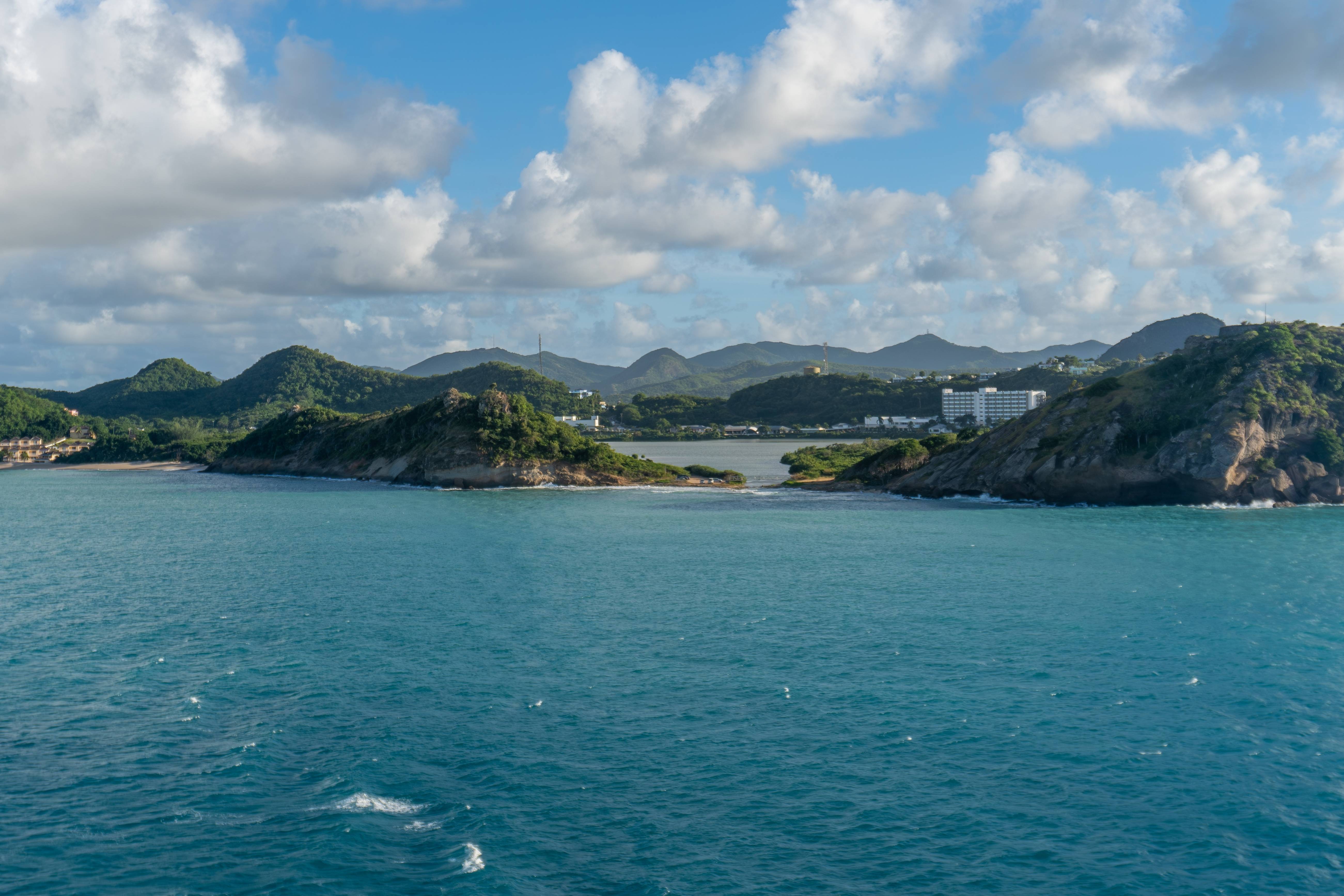 Lush green hills meet the turquoise waters of the Caribbean Sea under a sky dotted with fluffy white clouds.
