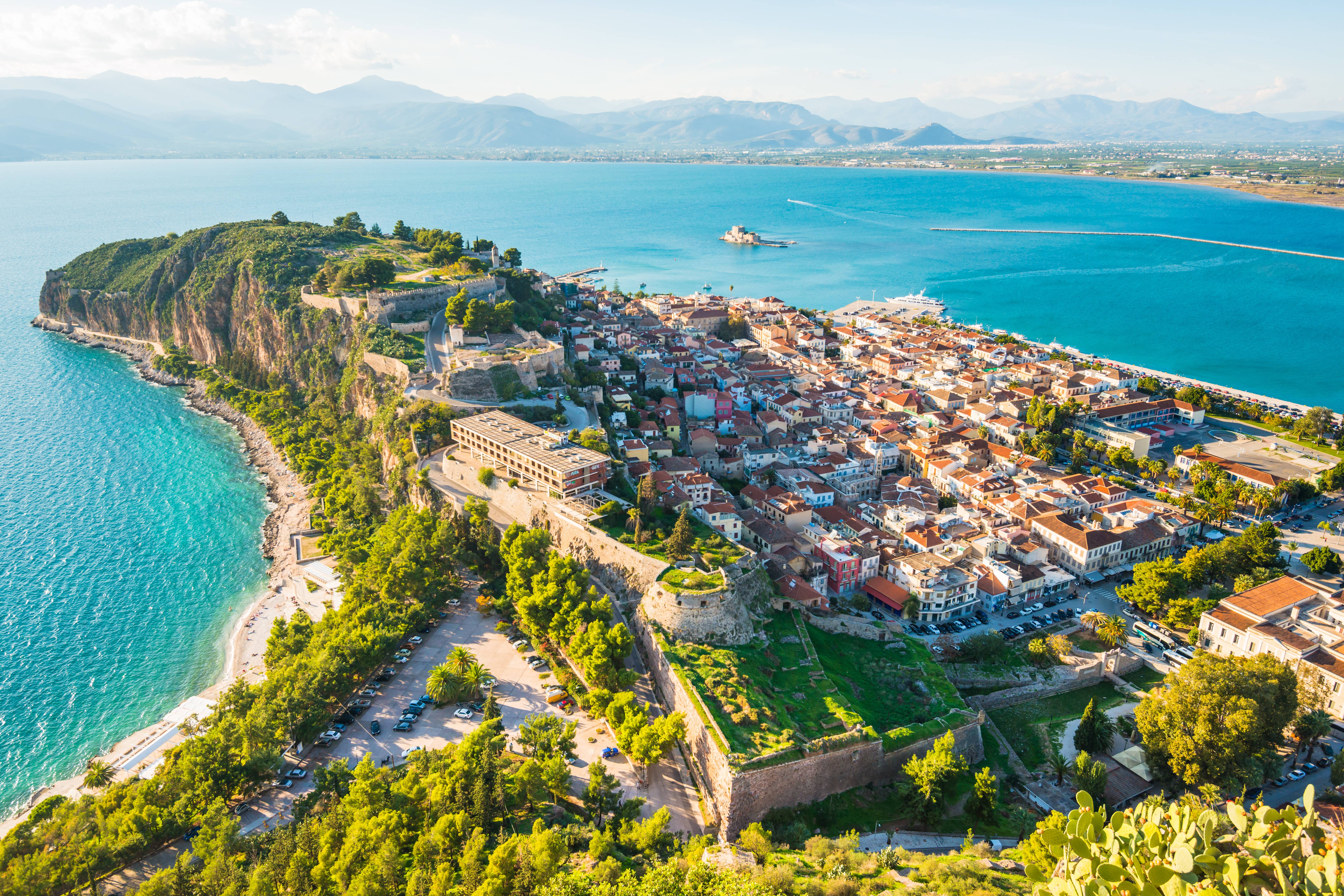 A picturesque coastal town unfolds beneath ancient fortifications overlooking the vibrant turquoise sea.