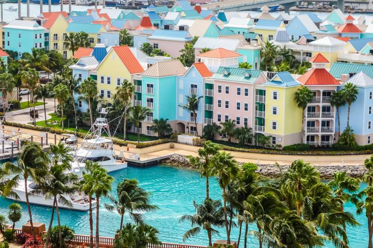 Pastel-colored buildings and lush palm trees line the vibrant turquoise waters of a tropical marina.