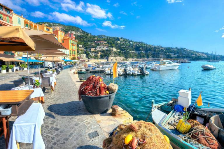 Colorful buildings line the harbor where fishing nets and boats await the day's catch under a bright blue sky.