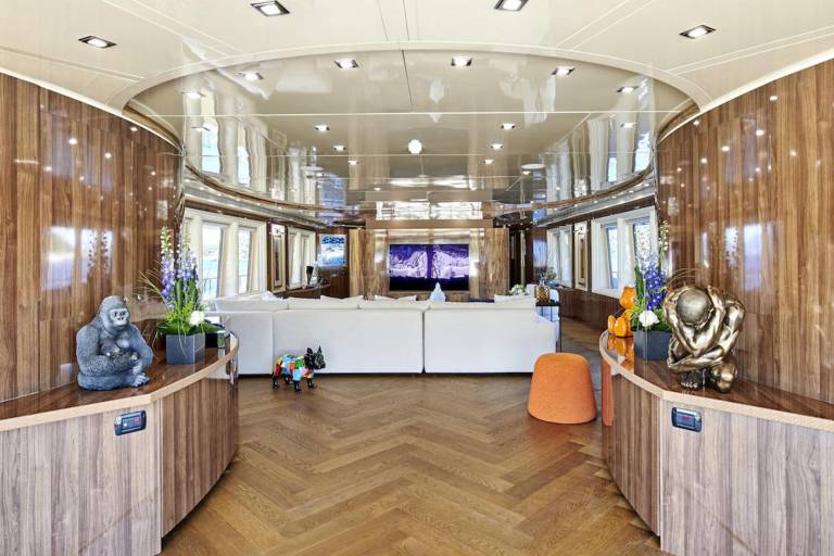 Luxurious yacht interiors feature rich wood paneling, plush white seating, and whimsical art pieces like a gorilla and a colorful dog statue.