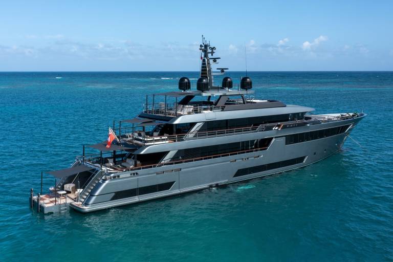 A sleek, modern yacht glides through the crystal-clear turquoise waters under a bright blue sky.