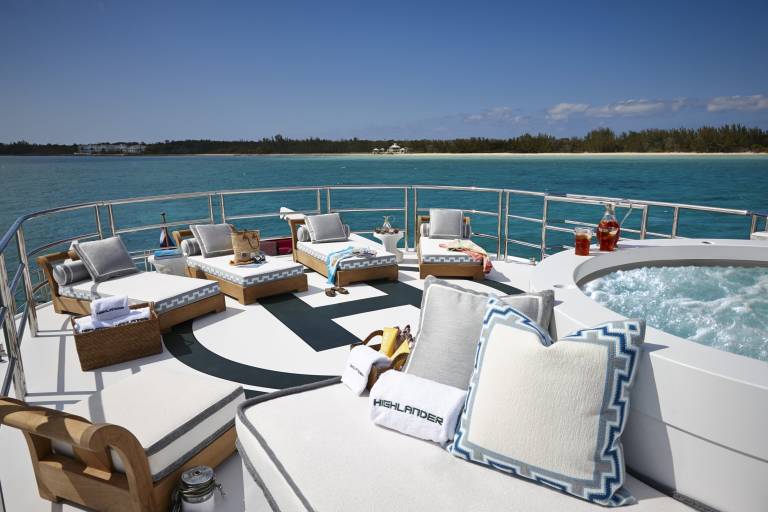 Relax on the deck of a luxury yacht, complete with comfortable loungers, a bubbling hot tub, and a tropical island backdrop.