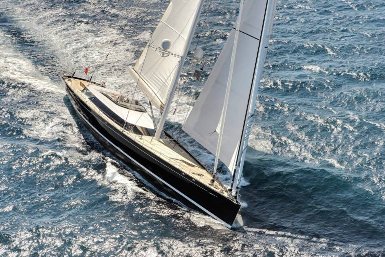 A sleek black yacht cuts through the sparkling blue ocean, its white sails billowing in the wind.