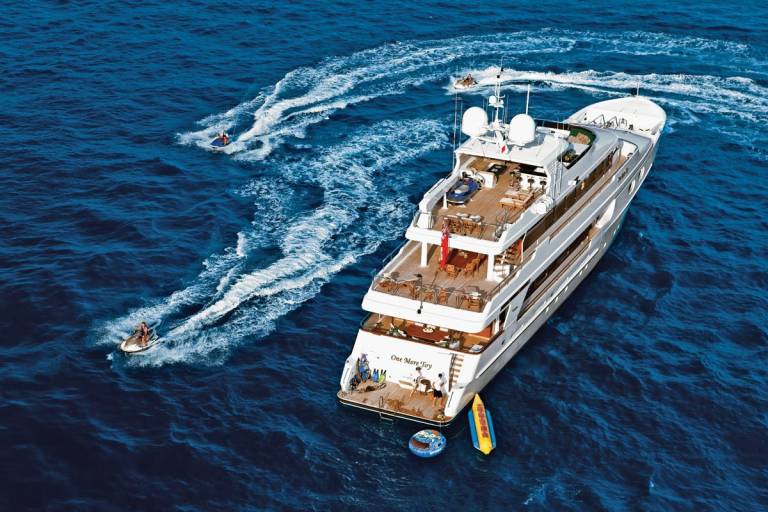 Jet skis create white wakes in the deep blue ocean as they race around a luxurious yacht.