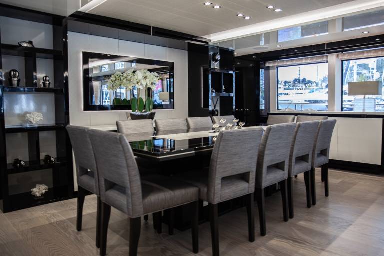 Elegant dining chairs surround a sleek table in a luxurious yacht interior with a view of the marina.