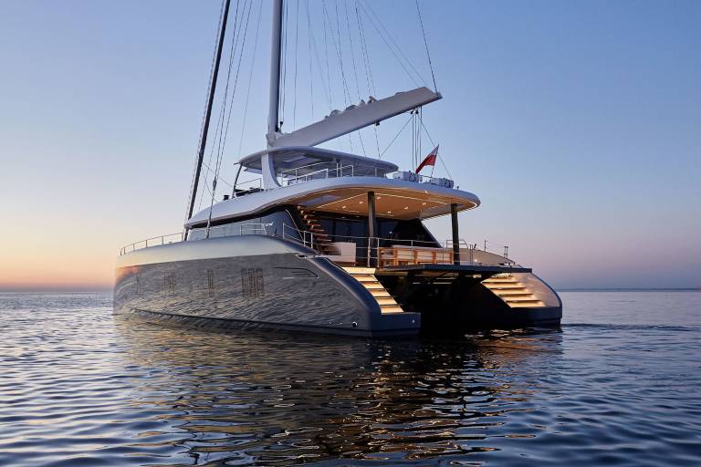 A sleek catamaran yacht glides across calm waters at dusk, its illuminated steps inviting exploration.