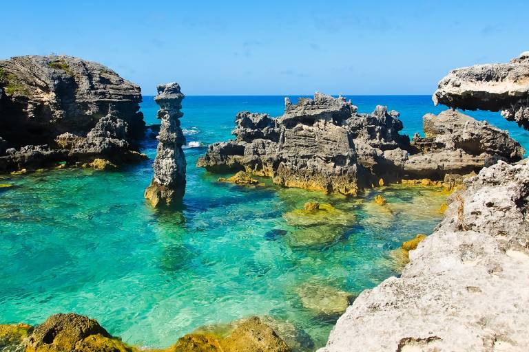 Dramatic rock formations rise from the crystal-clear turquoise waters under a brilliant blue sky.