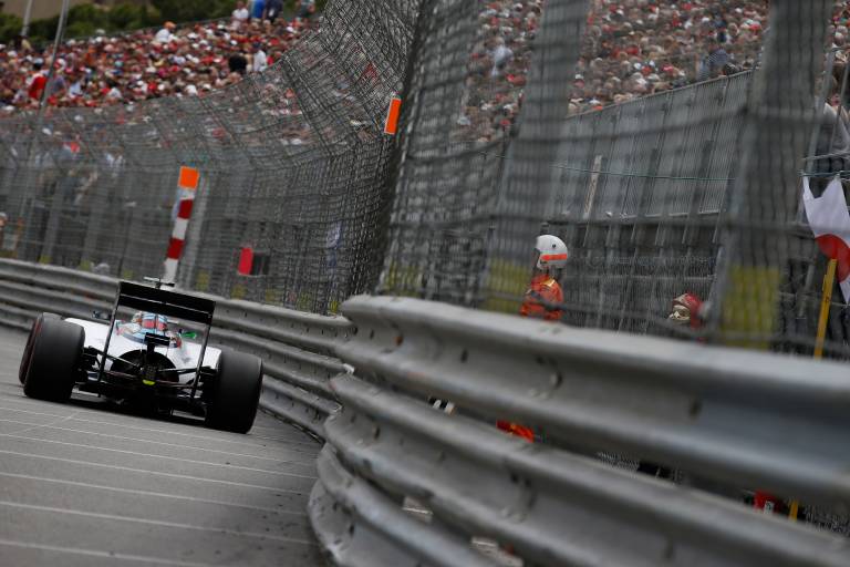 A Formula 1 car speeds around a corner as spectators fill the grandstands behind a protective fence.