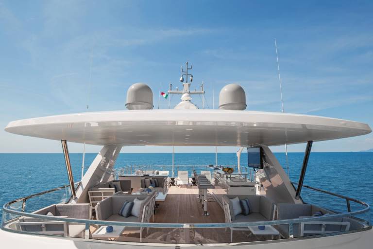 A large, white yacht with a sleek, modern design sits on the calm, blue ocean, with a clear sky in the background.