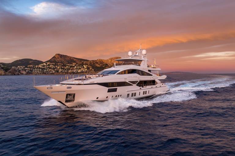 A luxurious white yacht glides through the deep blue sea at sunset, leaving a foamy wake against a dramatic sky.