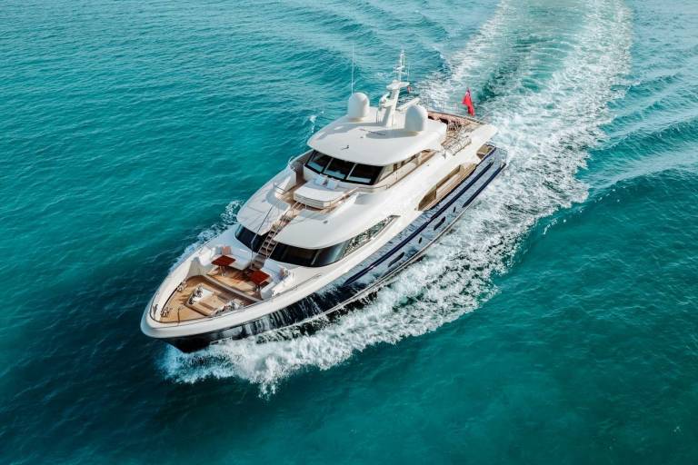 A luxurious yacht glides through turquoise waters, leaving a frothy white wake in its path.