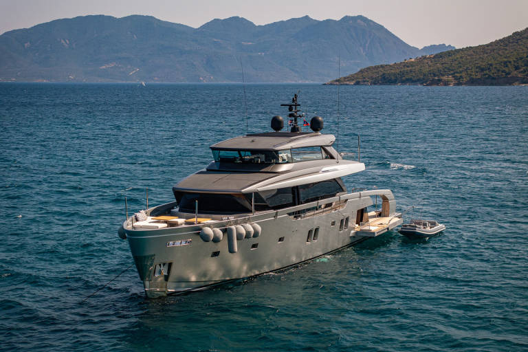 A sleek, modern yacht anchors in the azure waters off a verdant, mountainous coastline.