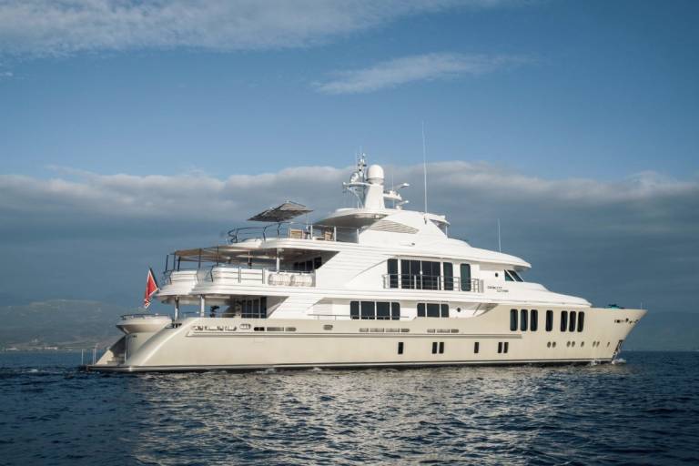 A luxurious yacht glides through calm blue waters under a partly cloudy sky.