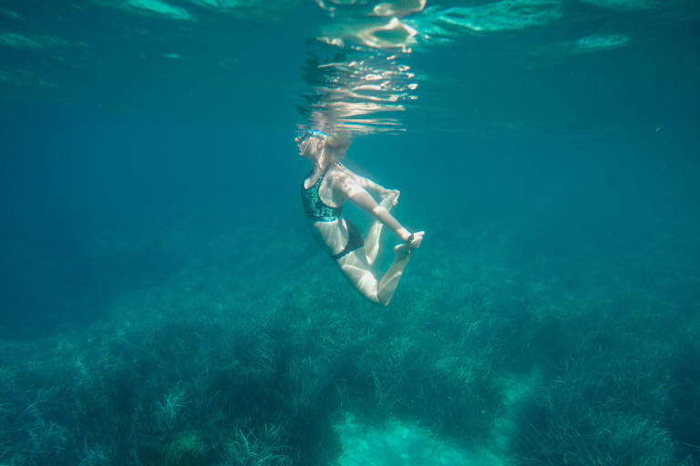 A woman in a swimsuit gracefully swims underwater above a bed of seagrass.