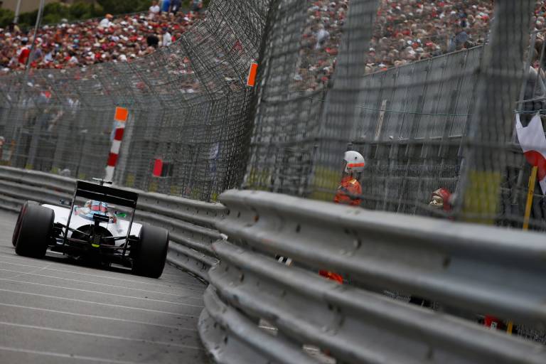 A race car speeds around a corner on a track with a large crowd of spectators in the background.