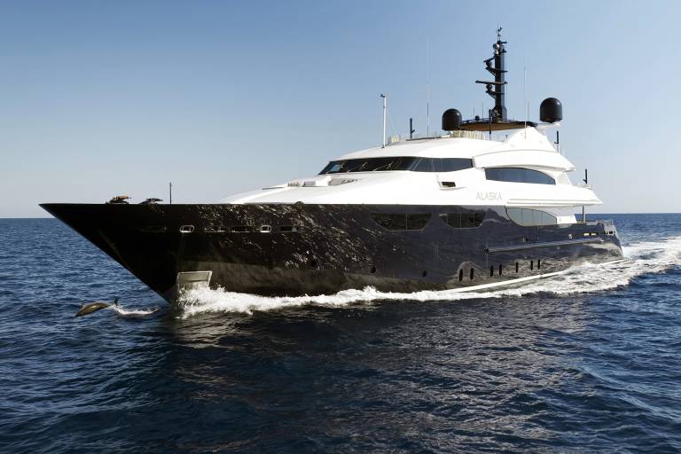 A large, sleek black and white yacht cuts through deep blue ocean waters under a clear, bright sky.