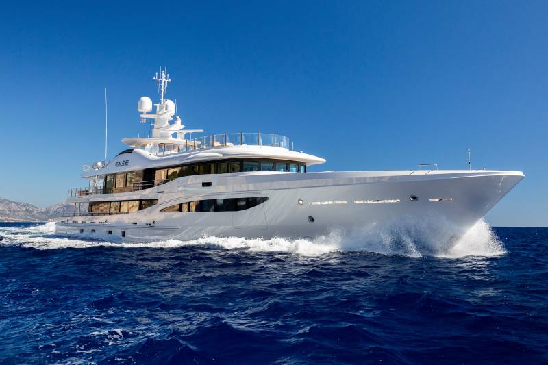 A sleek white yacht cuts through the deep blue ocean, leaving a trail of white spray against a clear sky.