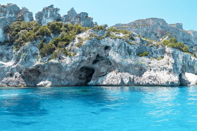 Azure waters lap at the base of rugged cliffs dotted with lush greenery and mysterious caves.