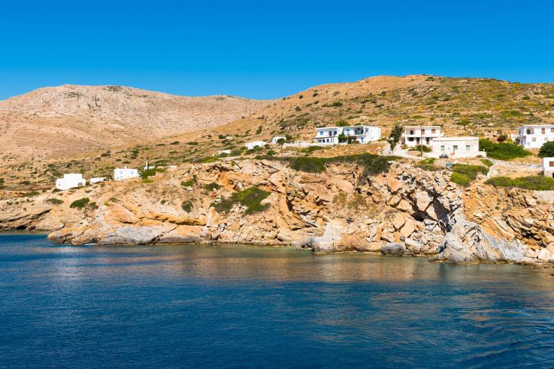 Whitewashed houses dot the rugged, sun-drenched hills overlooking the deep blue Aegean Sea.