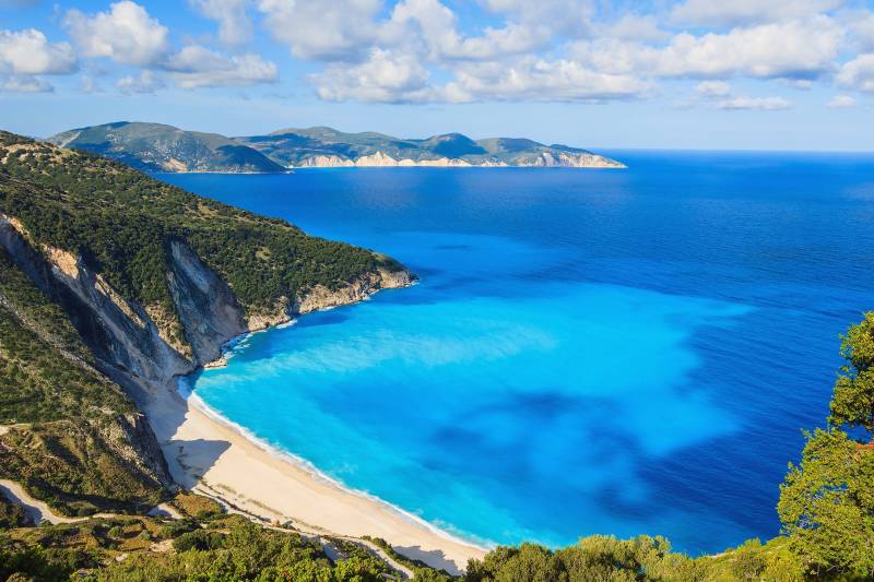 A winding road leads to the stunning turquoise waters and white sand beach of Myrtos Bay on Kefalonia, Greece.