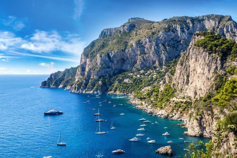Boats dot the azure waters surrounding the dramatic cliffs of Capri, a picturesque Italian island.
