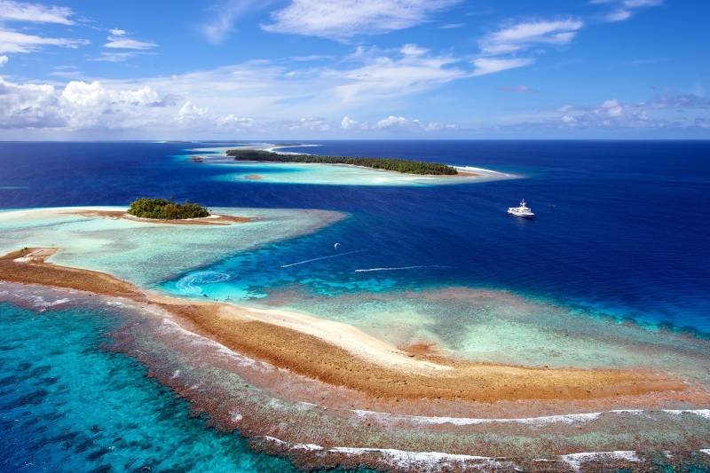 A luxurious yacht cruises through the turquoise waters of a tropical atoll, surrounded by lush green islands and vibrant coral reefs.