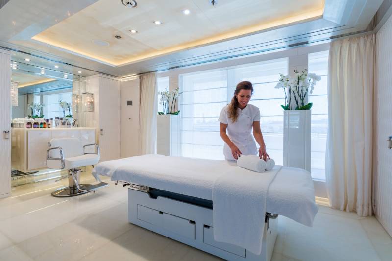 A spa attendant prepares a massage table with fresh towels in a luxurious, sunlit room.