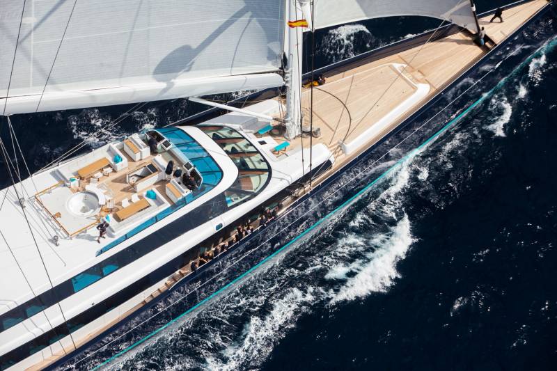 A luxurious yacht glides through the deep blue ocean, its sails catching the sunlight as passengers relax on deck.