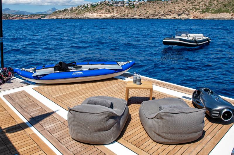 Relax on the deck of a luxury yacht with inflatable kayaks, a seabob, and comfortable seating, ready for aquatic adventures.