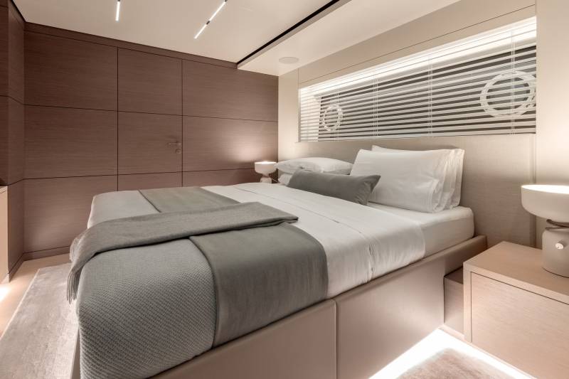 A luxurious yacht bedroom features a plush bed with grey throws and a modern bedside lamp.