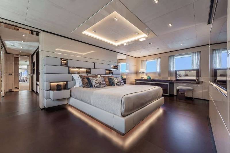 A luxurious yacht bedroom features a plush bed, modern headboard, and elegant mirrored accents.