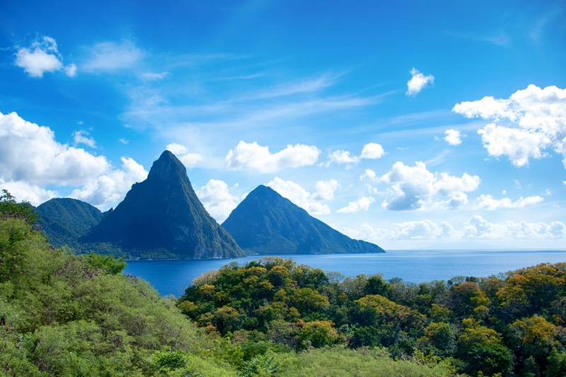 The iconic Pitons rise majestically from the turquoise waters of St. Lucia, framed by lush green foliage under a brilliant blue sky.