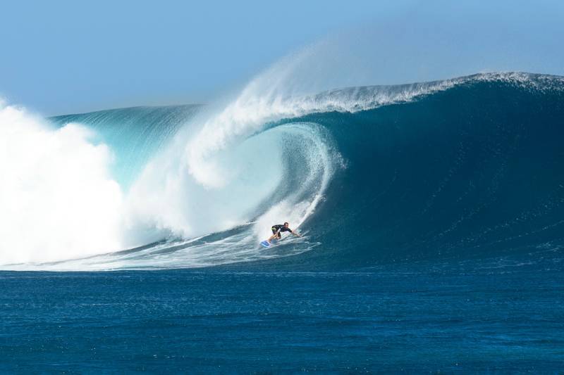 A lone surfer carves through a colossal wave, a breathtaking display of power and grace against the vast blue ocean.