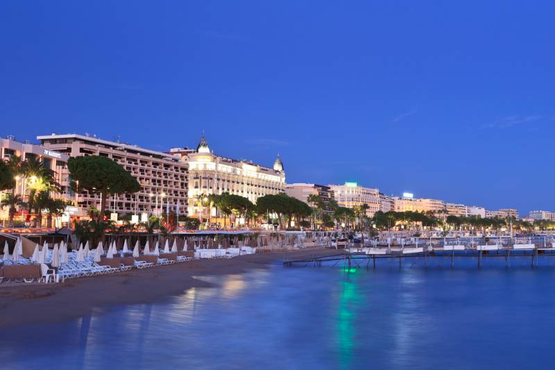 The vibrant lights of Cannes hotels illuminate the beach and sea at dusk.