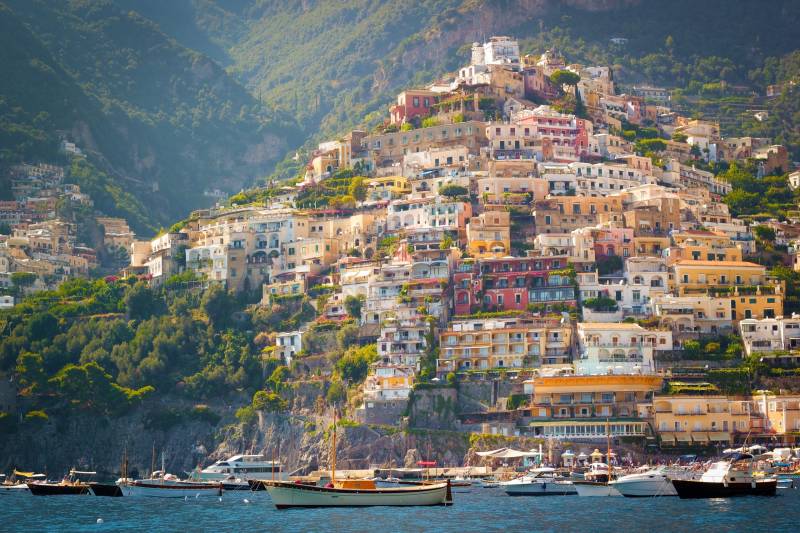 Colorful buildings cascade down a steep hillside to the sparkling blue waters of the Amalfi Coast.