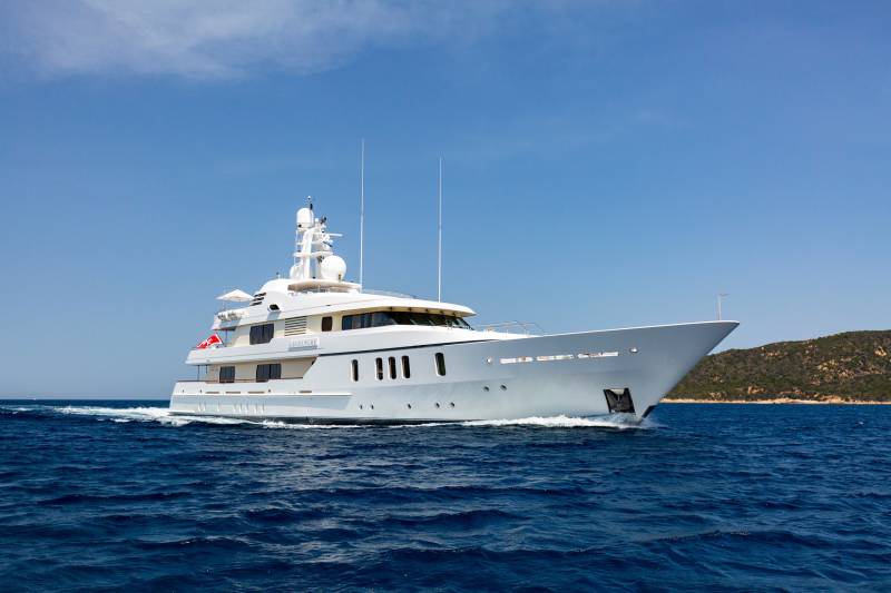 A luxurious white yacht named Adventure cruises through the deep blue ocean under a clear sky.