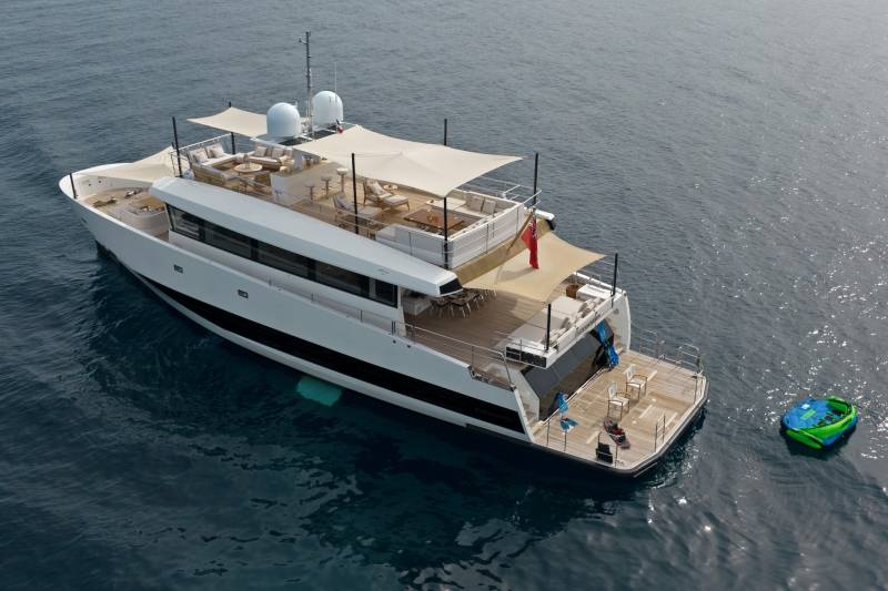A luxurious white yacht with ample deck space for relaxation floats serenely on the calm blue sea.