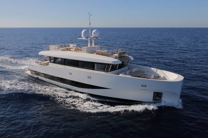 A sleek white superyacht glides through the deep blue ocean on a clear, sunny day.
