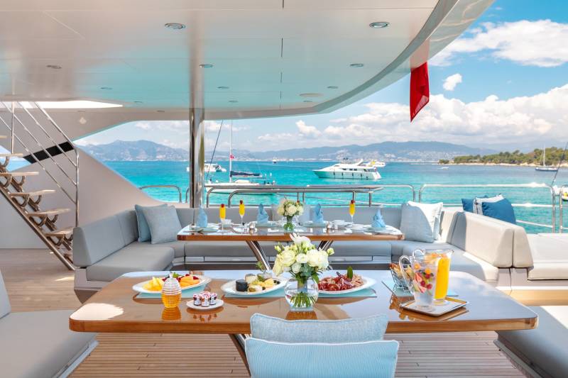 A luxurious yacht deck is set for a delightful meal with stunning ocean views and a spread of fresh fruit, cheese, and drinks.