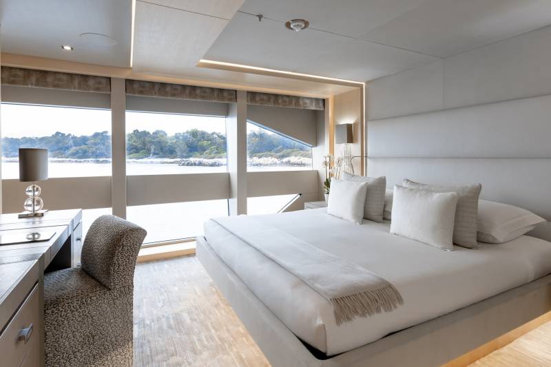 Luxurious yacht stateroom offers serene ocean views from a plush bed and elegant desk area.