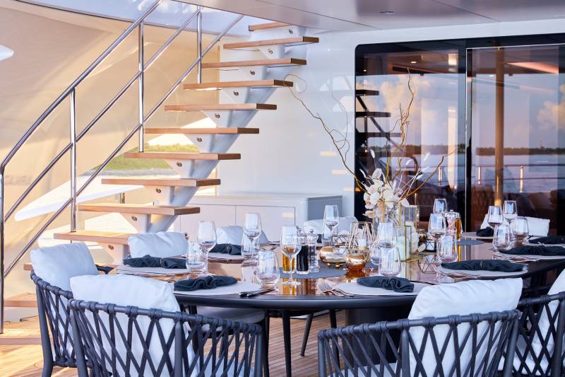 An elegant yacht deck dining setting awaits guests with a beautifully laid table and a scenic water view.