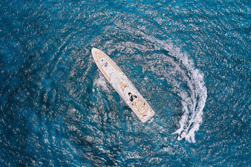 A luxurious yacht glides through the vibrant blue ocean, leaving a trail of white wake behind it.
